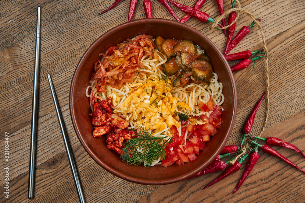 Φωτογραφία Traditional Korean wok noodles with hot pepper, meat, shiitake mushrooms and omelet in a ceramic plate on a wooden background