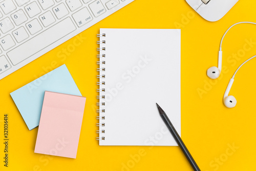 Blank spiral notepad with keyboard, supplies and pencil on bright yellow background. Top view office desk with notepad. Creative flat lay photo