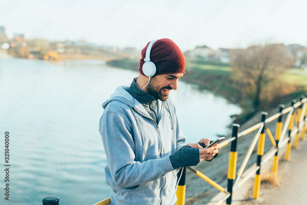young man jogging outdoors on street, using mobile phone