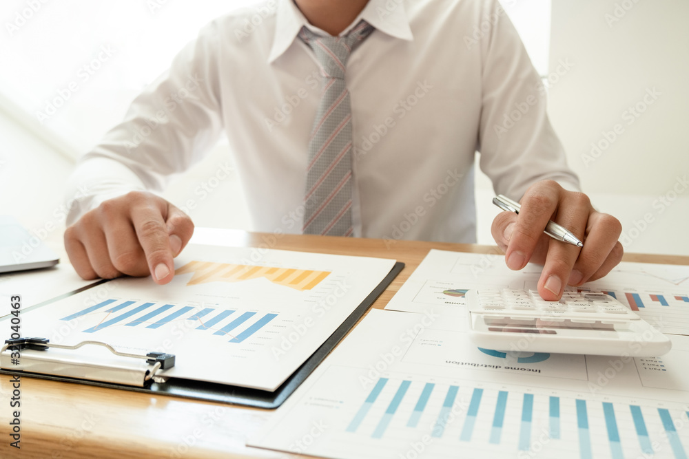 A business man is sitting at a desk and calculating financial graphs about real estate investment expenditures A business man is sitting at a desk and calculating financial graphs about real estate investment expenditures
