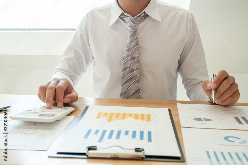 A business man is sitting at a desk and calculating financial graphs about real estate investment expenditures A business man is sitting at a desk and calculating financial graphs about real estate investment expenditures