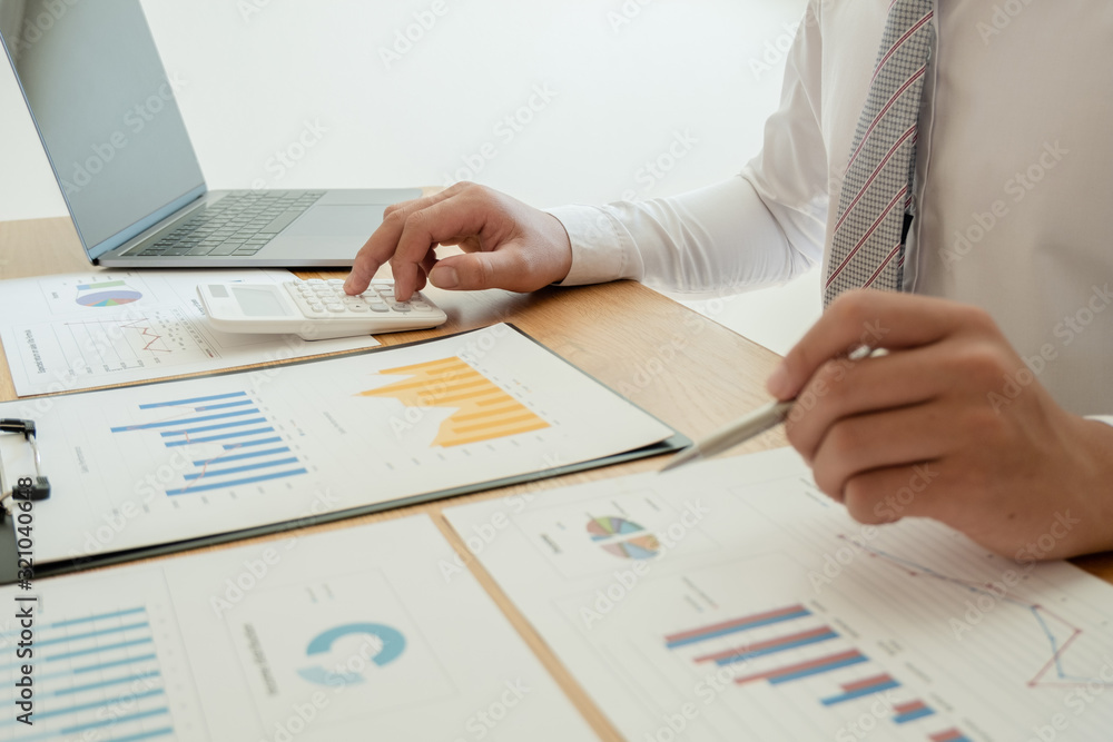 A business man is sitting at a desk and calculating financial graphs about real estate investment expenditures A business man is sitting at a desk and calculating financial graphs about real estate investment expenditures