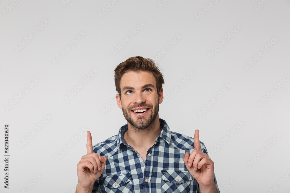 Portrait of joyful young man smiling and pointing fingers upward Portrait of joyful young man smiling and pointing fingers upward