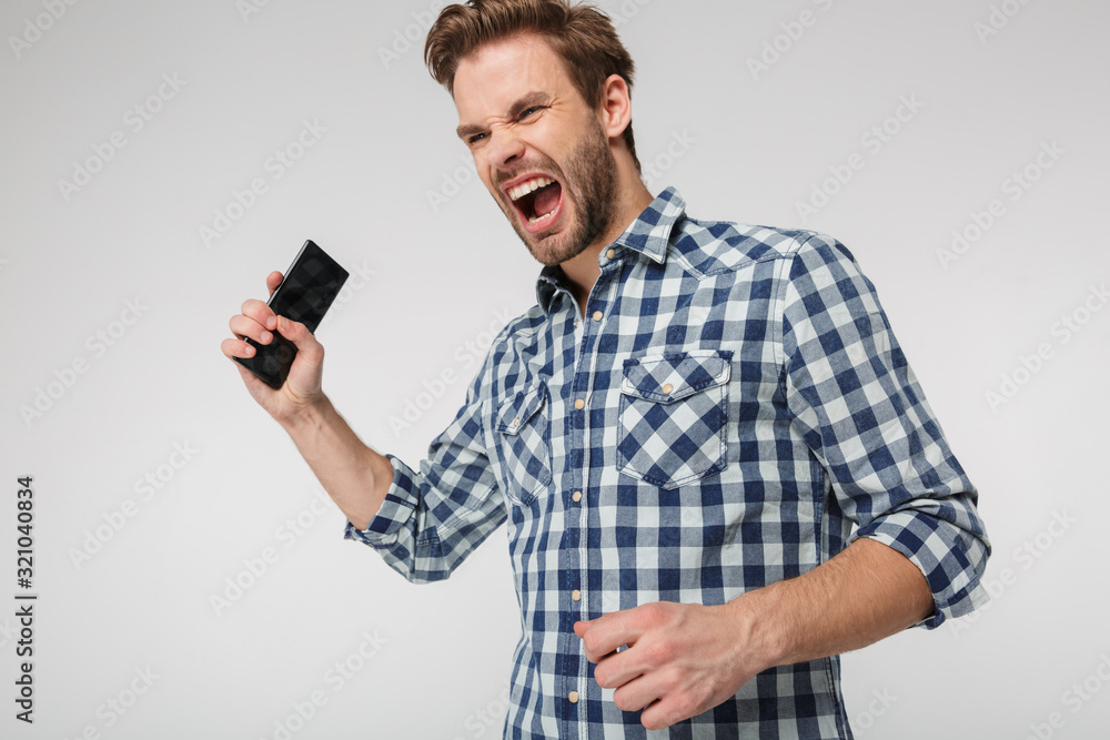 Portrait of angry young man screaming and holding cellphone Portrait of angry young man screaming and holding cellphone