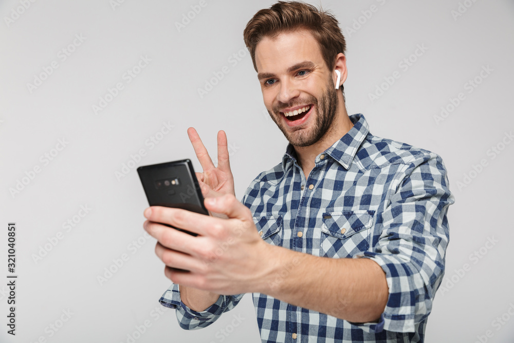 Portrait of happy young man gesturing peace sign while using cellphone Portrait of happy young man gesturing peace sign while using cellphone