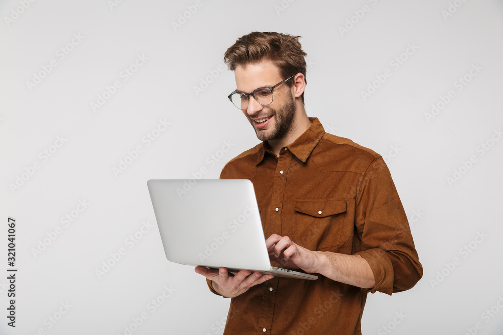 Portrait of cheerful young man using laptop and smiling - obrazy, fototapety, plakaty 