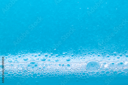 Transparent foaming blue liquid with oxygen bubbles texture close up. Abstract surfactant cosmetic background. SLS free concept photo