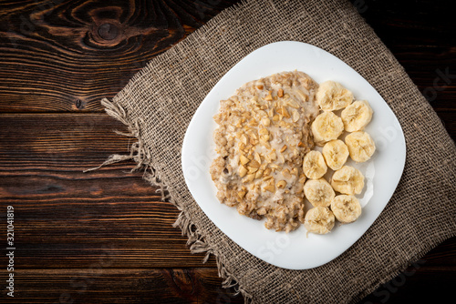 Oatmeal with banana and peanut on dark wooden background.