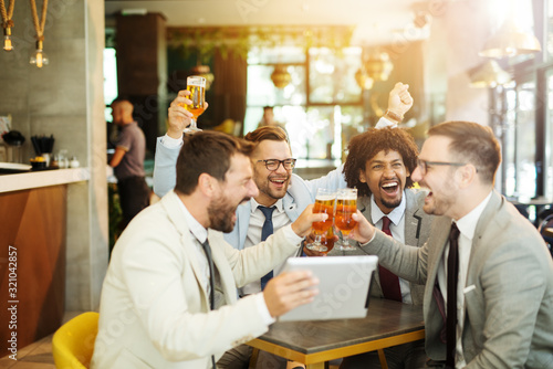 Happy creative business colleagues having a drink after work and using tablet