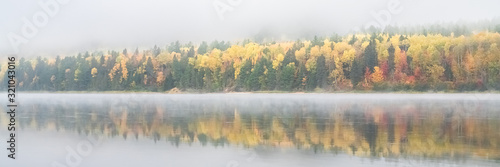A lake in the forest in Canada, during the Indian summer, with fog on the water in the morning