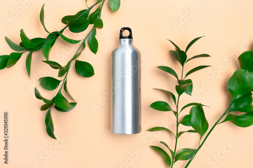 Metal bottle and frame made of ruscus branches. Zero waste concept on yellow background.