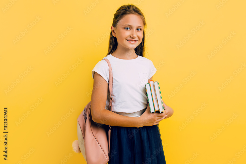 A teenager with a backpack and books. Stylish beautiful schoolgirl posing on a yellow background - obrazy, fototapety, plakaty 