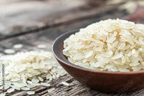 A bowl of white rice against the background of old boards near sprinkled rice. Jasmine rice for cooking.