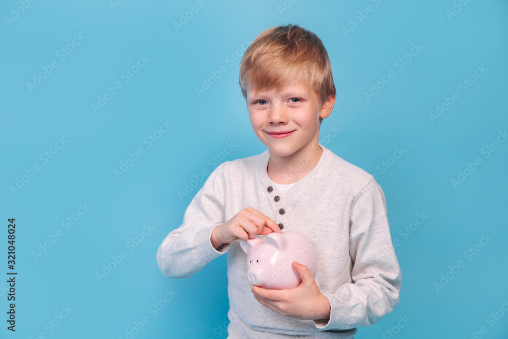 Little boy saving money in a piggybank on blue background Little boy saving money in a piggybank on blue background