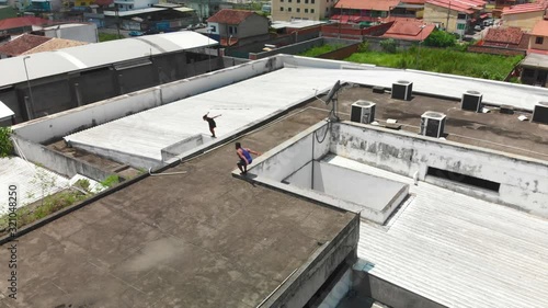 two young freeruners jumping and performing  flips and tricks over obstacles on a rooftop followed bya drone photo