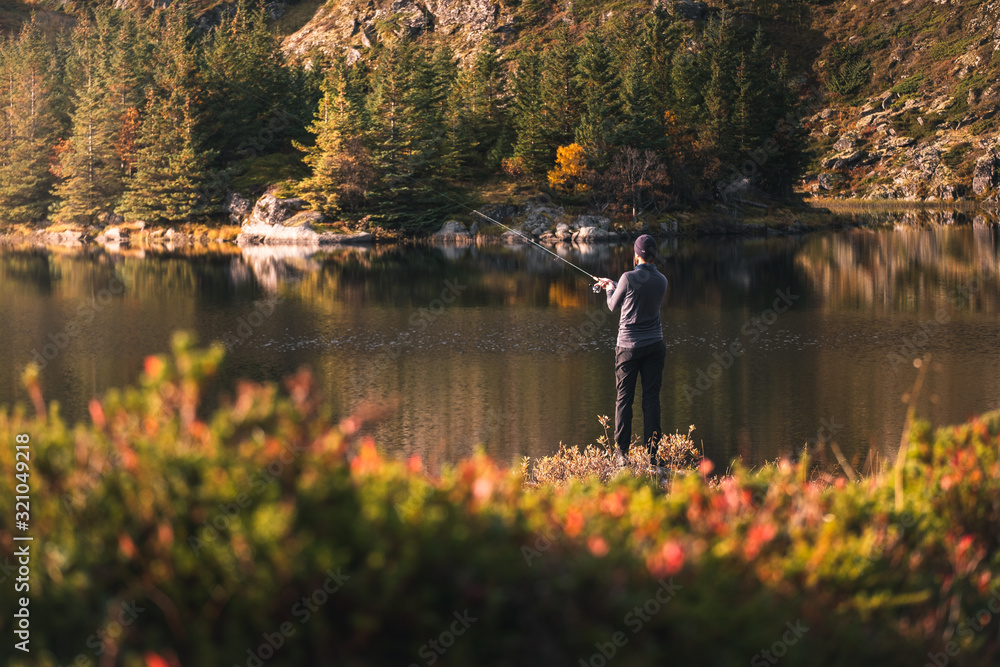 Obraz premium Fishing as recreation and sports displayed by fisherman at lake. Fishing during sunlight in beautiful landscape and mountain in background.