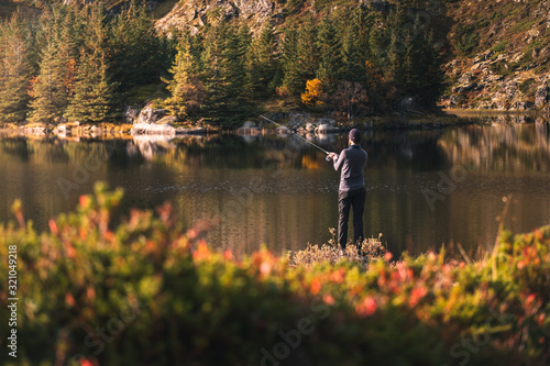 Fishing as recreation and sports displayed by fisherman at lake. Fishing during sunlight in beautiful landscape and mountain in background.