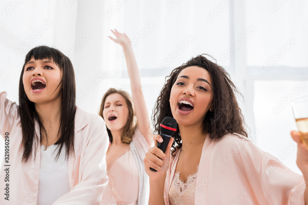 beautiful smiling multicultural girls singing with microphone on pajama party beautiful smiling multicultural girls singing with microphone on pajama party