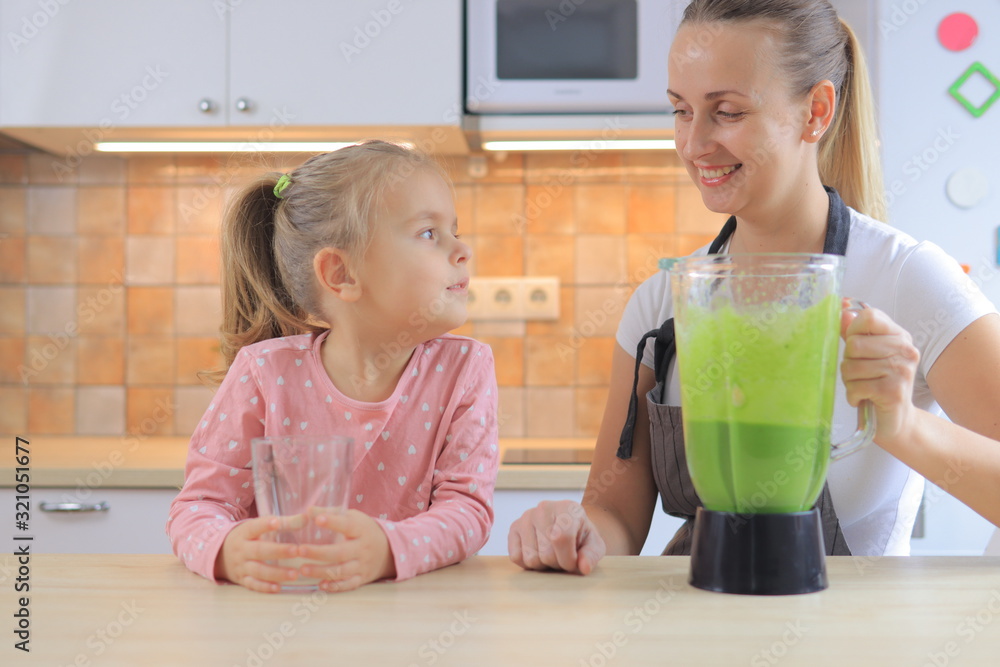 Mother pouring healthy green smoothie to glass for her daughter Mother pouring healthy green smoothie to glass for her daughter