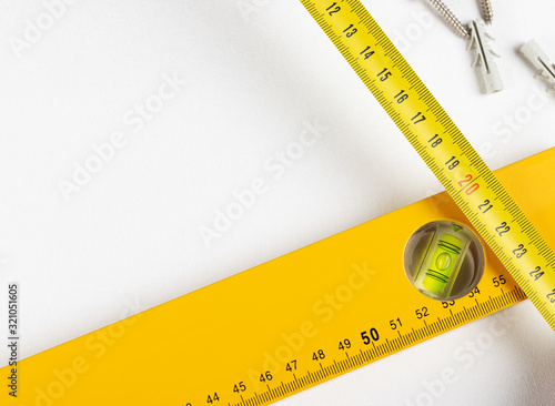 Yellow tape measure spirit level and scaffolding dowels and self-tapping screws on clear white background. Horizontal photo. Place for text.