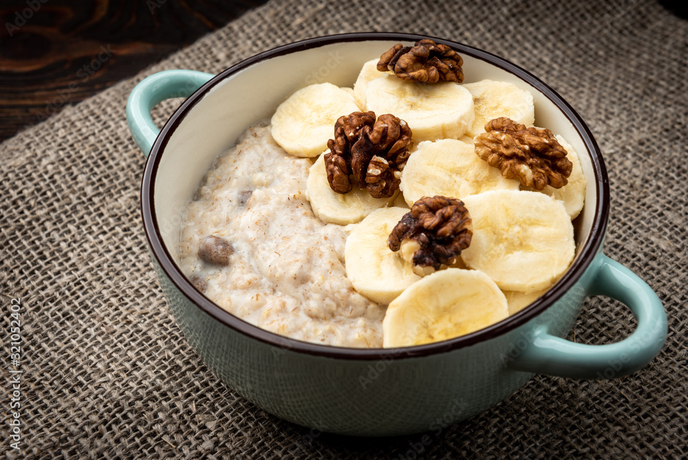 Oatmeal with banana and walnut in green bowl on dark wooden background. Oatmeal with banana and walnut in green bowl on dark wooden background.
