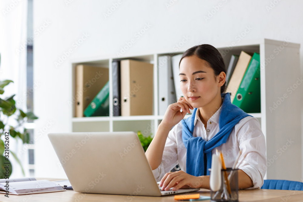 Image of young asian woman using laptop computer while working in office Image of young asian woman using laptop computer while working in office