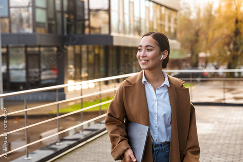 Obraz na plátně Image of young brunette asian woman holding laptop while walking