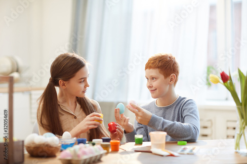 Two children sitting at the table and painting eggs for Easter together