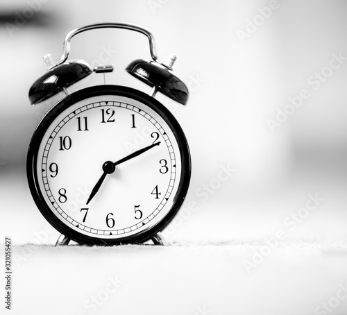 Still life black vintage alarm clock shows 7 am on bright bokeh background with copy space. Retro alarm clock