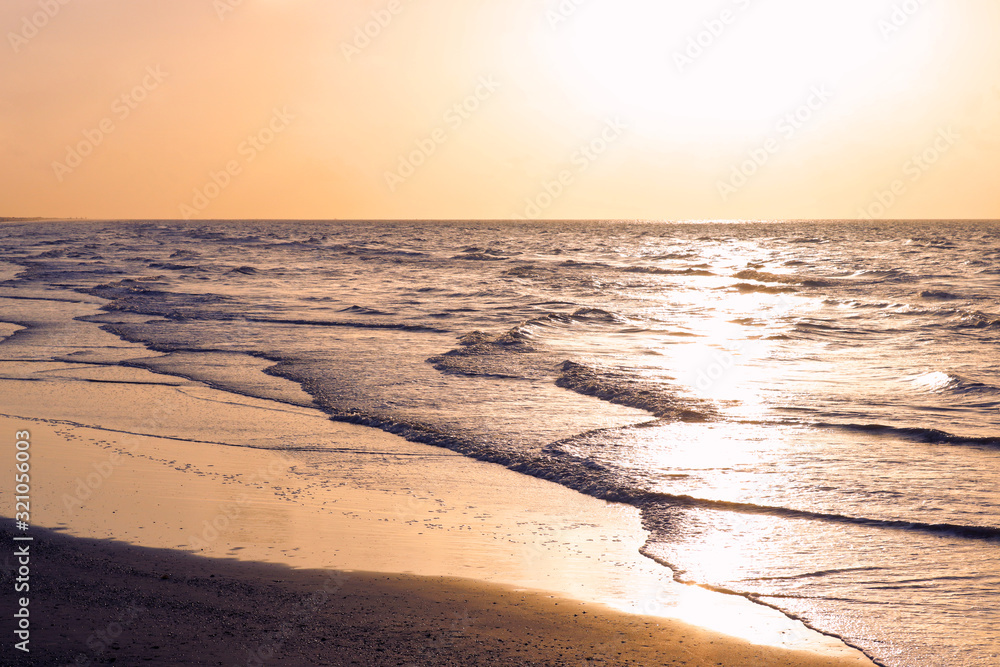 Sunrise on the beach. Gentle waves hit the shore as the sun rises over the sea. Travel and tourism landscape background with copy space.