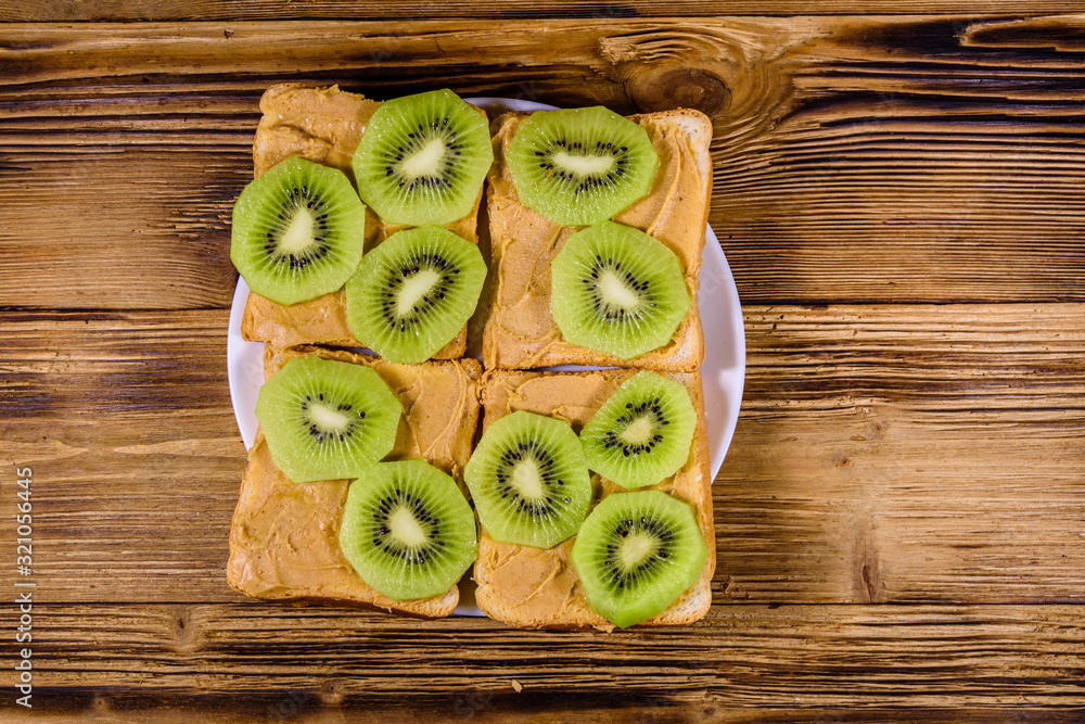 Sandwiches with peanut butter and sliced kiwi fruits in plate on a wooden table. Top view Sandwiches with peanut butter and sliced kiwi fruits in plate on a wooden table. Top view