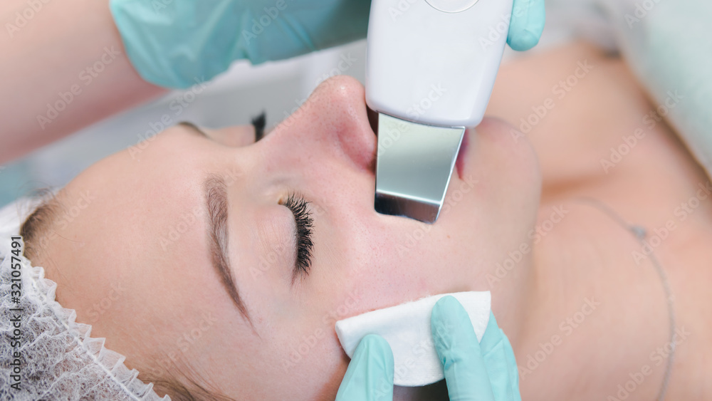 Fototapeta premium The female cosmetologist makes a procedure of ultrasonic cleaning face, close-up. Young woman in a beauty salon.