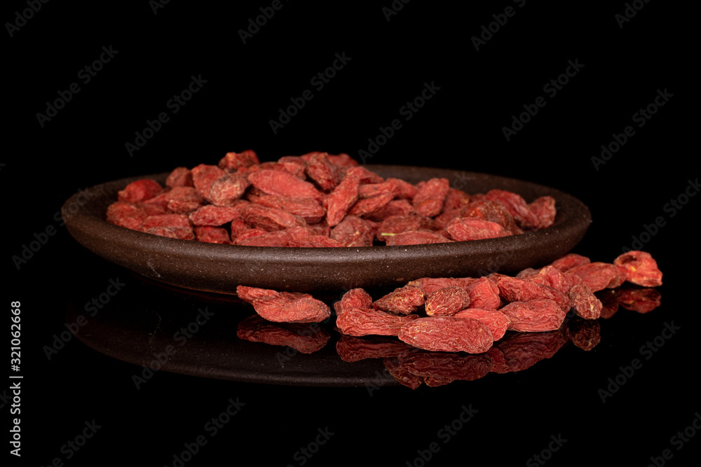 Lot of whole dried red goji berries with brown ceramic coaster isolated on black glass Lot of whole dried red goji berries with brown ceramic coaster isolated on black glass
