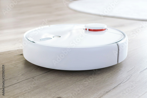White robot vacuum cleaner on laminate floor. Modern smart device cleaning floor.