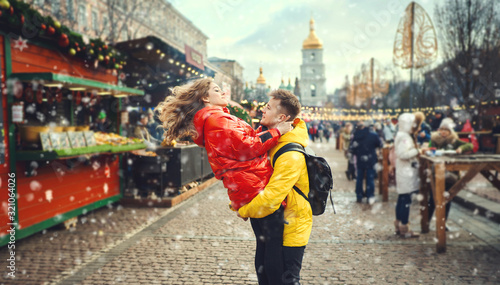 Young couple having fun together at snowy day and looking happy, handsome young man carrying his girlfriend while walking on the street.