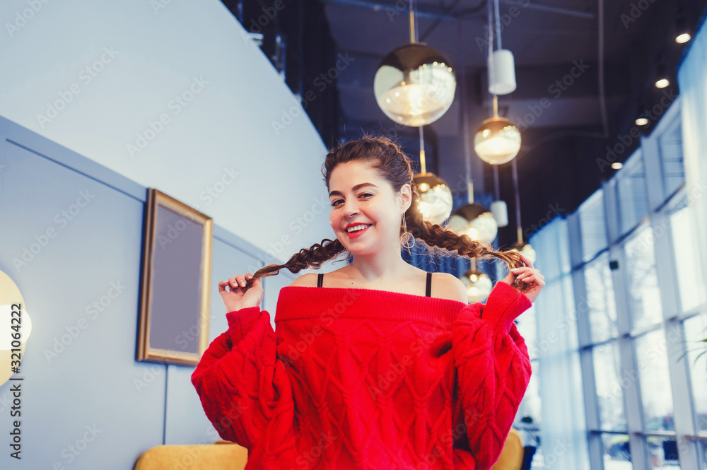 portrait of a positive smiling girl with pigtails and a red sweater in the room