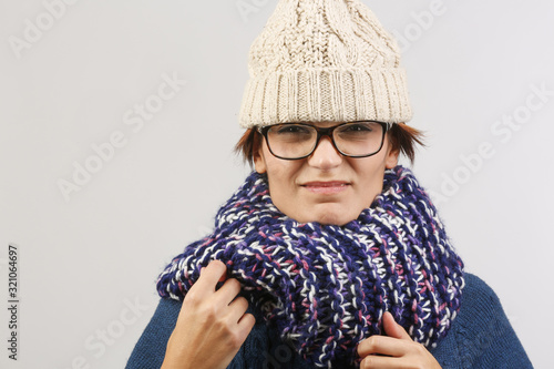 Ragazza bruttina con cuffietka e sciarpa si tiene gli occhiali, isolata su sfondo chiaro photo