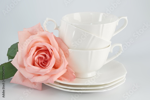 White porcelain cup with a saucer for tea or coffee and pink rose, demitasse or teacup. Crockery on white background.