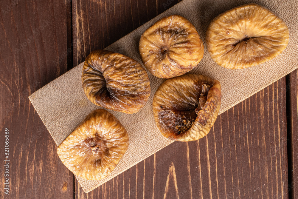 Group of five whole dried fig on wooden cutting board flatlay on brown wood Group of five whole dried fig on wooden cutting board flatlay on brown wood