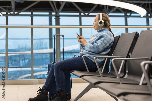 A girl at the airport waiting for departure sits in headphones listening to music in the waiting room