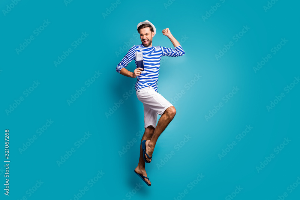 Full length profile photo of funky guy tourist jump high celebrating vacation start getting visa wear striped sailor shirt vest cap shorts flip flops isolated blue color background Full length profile photo of funky guy tourist jump high celebrating vacation start getting visa wear striped sailor shirt vest cap shorts flip flops isolated blue color background