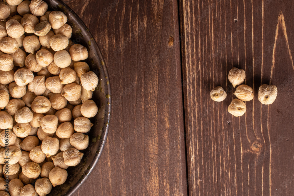 Fototapeta premium Lot of whole fresh tan chickpea in glazed bowl flatlay on brown wood