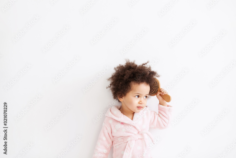 Cute little girl in soft bathrobe brushing her curly hair Cute little girl in soft bathrobe brushing her curly hair