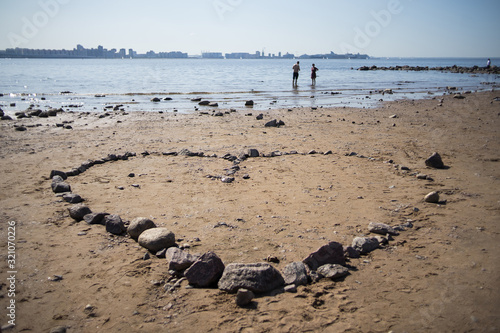 Fototapeta Naklejka Na Ścianę i Meble -  Stoned heart on the beach. Against the background of a young couple in love