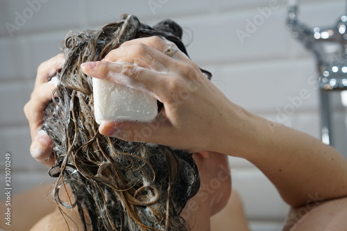 Caucasian woman washes her brown hair with shampoo bar or soap, zero waste concept