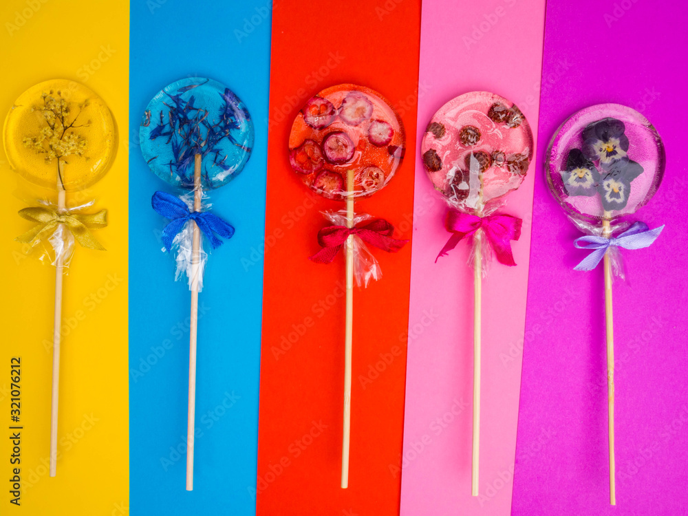 Handmade flat round lollipops with flowers and berries inside on colorful background. Elder, violet, cornflower, raspberries, cranberries, wild strawberries, Herbs and berries. Health concept Handmade flat round lollipops with flowers and berries inside on colorful background. Elder, violet, cornflower, raspberries, cranberries, wild strawberries, Herbs and berries. Health concept