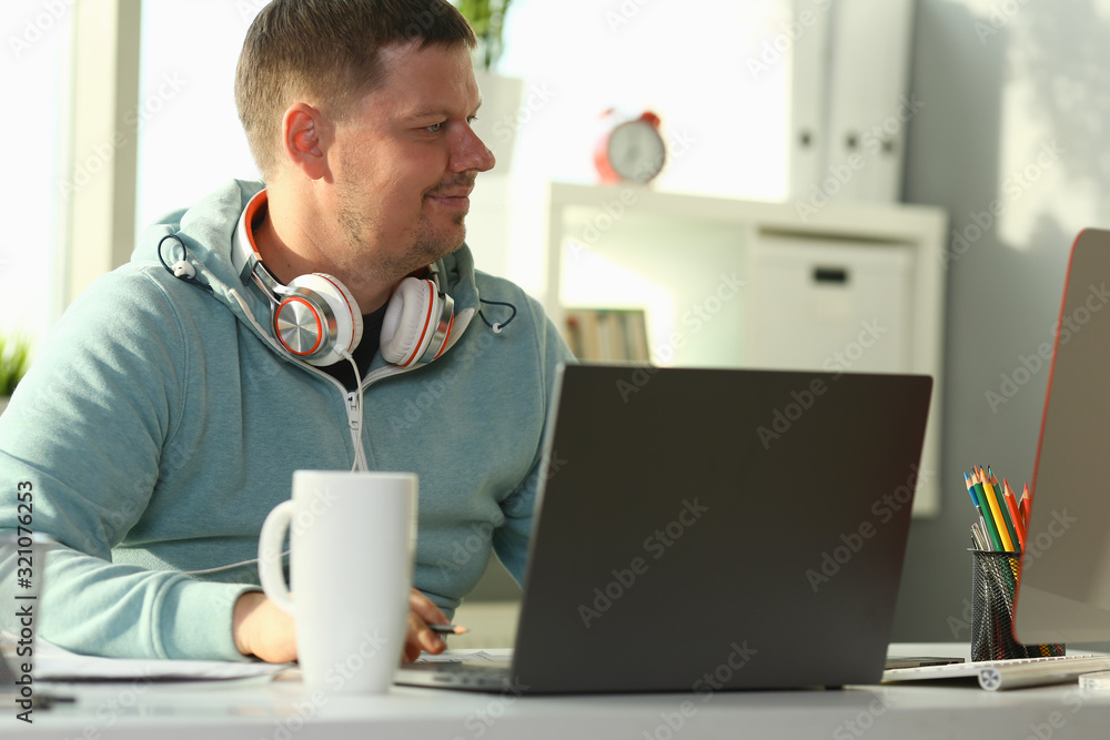 Handsome smiling male student using online education service. Young man looking in laptop display watching training course and listening it with headphones. Modern study technology concept Handsome smiling male student using online education service. Young man looking in laptop display watching training course and listening it with headphones. Modern study technology concept