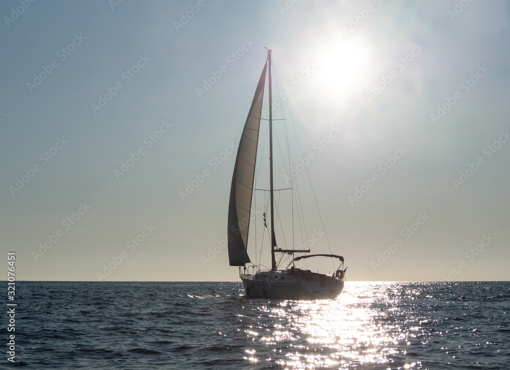 Silhouette of sailing yacht on glowing sea water at sunset background