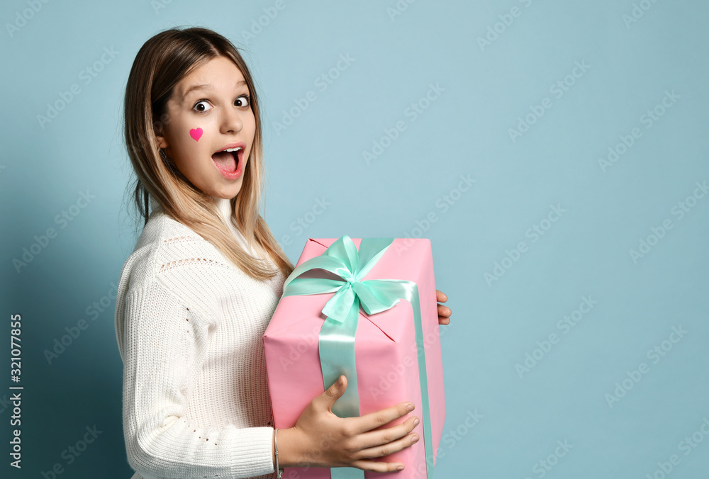 Much surprised teen kid girl celebrate valentines day holding a big pink present gifts box for birthday. Much surprised teen kid girl celebrate valentines day holding a big pink present gifts box for birthday.