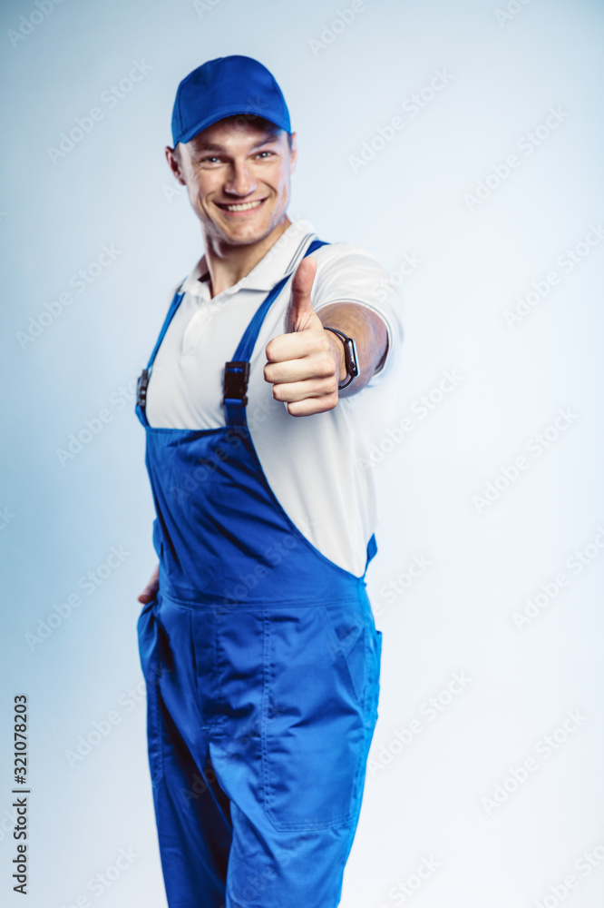 Portrait of young worker man wearing blue uniform. Showing thumb up. Movement cool. Isolated on grey background with copy space. Human face expression, emotion. Business concept.